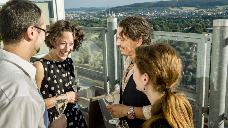© JenaKultur, Foto: Andreas Hub Personen auf der Ausichtsplatform des JenTower trinken ein Glas Sekt mit der Stadt im Hintergrund © JenaKultur, Foto: Andreas Hub