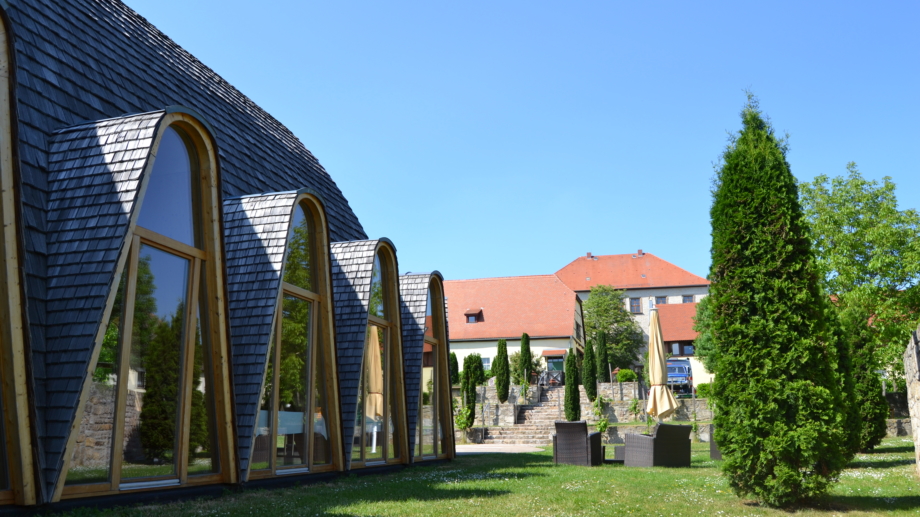 Quelle: Landratsamt Weimarer Land, Foto: Katy Kasten-Wutzler Weltdorfgemeinschaftshaus Maloca im Garten mit Sitzecken und Blick zum Schloss Auerstedt